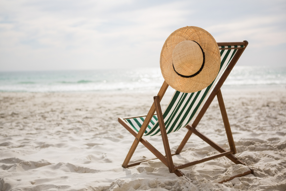 Silla de playa en la arena, junto a un sombrero para el sol